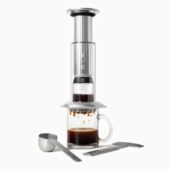 Cafetière AeroPress avec tasse et accessoires en acier inoxydable.