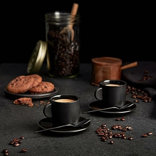 Deux tasses de café noir avec des biscuits et des grains de café sur fond sombre.
