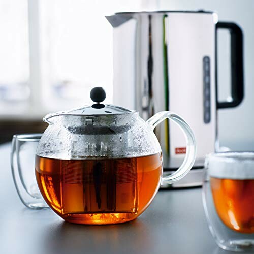 Théière en verre avec thé infusé et bouilloire électrique en arrière-plan.
