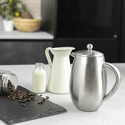 Cafetière en acier inoxydable avec grains de café et lait.